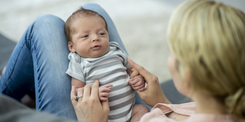 Neugeborenes Baby mit gestreiftem Strampler auf dem Schoss von Mama