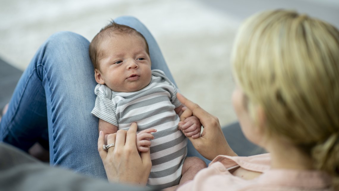 Neugeborenes Baby mit gestreiftem Strampler auf dem Schoss von Mama