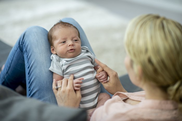 Neugeborenes Baby mit gestreiftem Strampler auf dem Schoss von Mama