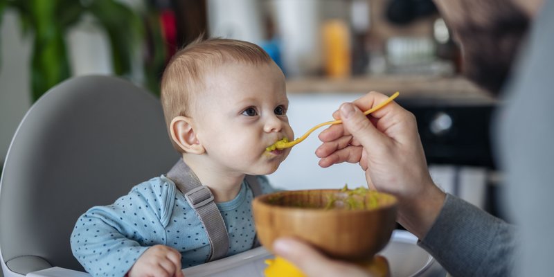 Baby auf Hochstuhl bekommt Brei von Papa