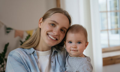 Junge Mama blickt freundlich mit Baby in die Kamera