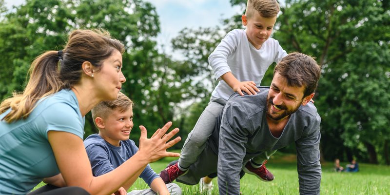 Familie spielt auf Wiese im Sommer, Kind sitzt auf Papas Rücken