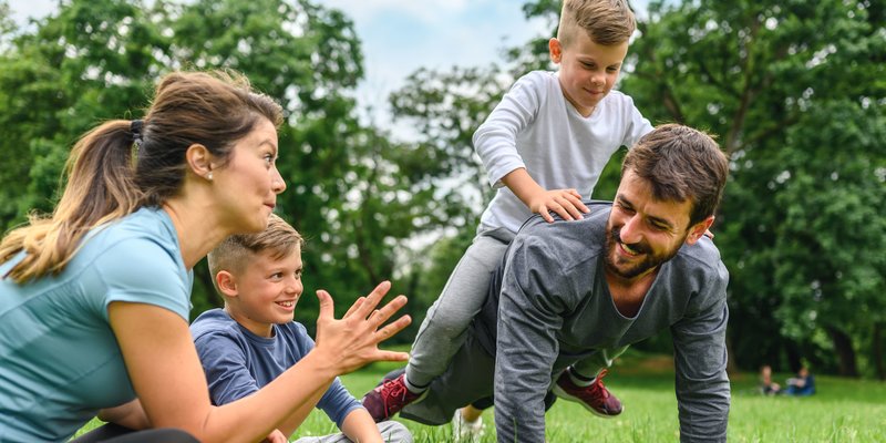 Familie spielt auf Wiese im Sommer, Kind sitzt auf Papas Rücken